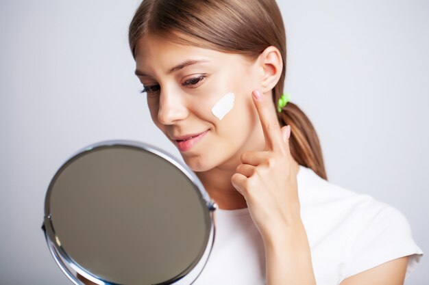 Vrouw gezicht huid cosmetica, vrouw voor een spiegel past een crème voor huidverzorging