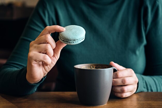 Vrouw gezichtsloos met koffiekopje en bitterkoekjes zit aan café tafel close-up Selectieve focus