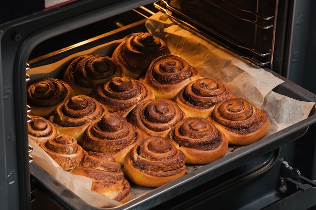 Vrouw haalt uit de oven smakelijke gebakken kaneelbroodjes met een blozende korst