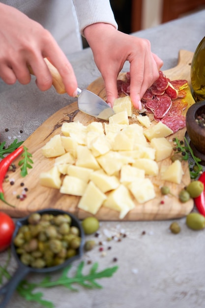 Vrouw hakt Parmezaanse kaas met mes op grijze tafel in de binnenlandse keuken