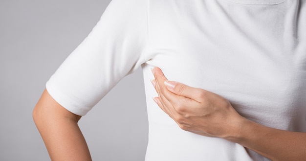 Vrouw hand controleren knobbels op haar borst op tekenen van borstkanker op grijze achtergrond. Gezondheidszorgconcept.