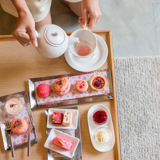 Vrouw hand gieten hete thee met Afternoon tea set en roze dessert in luxehotel