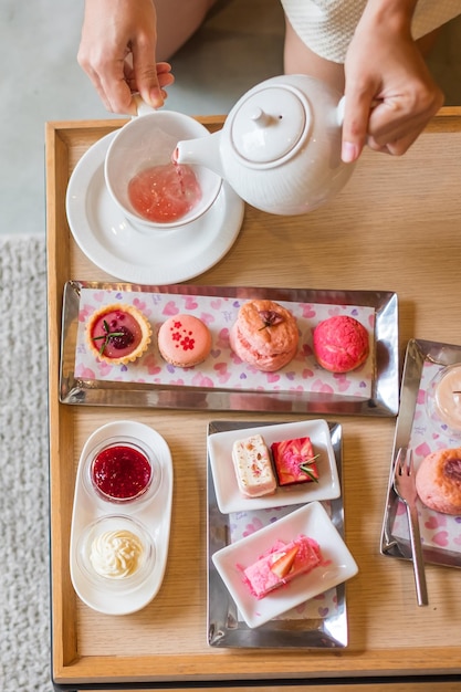 Vrouw hand gieten hete thee met Afternoon tea set en roze dessert in luxehotel