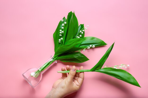 Vrouw hand houdt een boeket van lelietje-van-dalen in de transparante glazen vaas en kleine tak t...