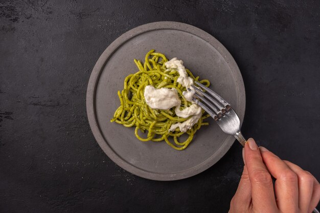 Vrouw hand houdt een vork met een pasta met strachatella en pesto, selectieve aandacht, bovenaanzicht