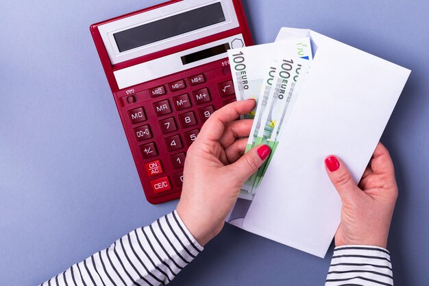 Vrouw hand in hand met een envelop met contant geld, rekenmachine, eurobankbiljetten.