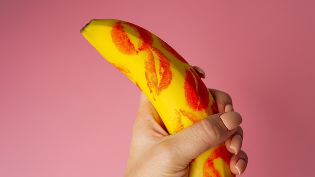 Vrouw hand met banaan met rode lippenstift markeringen op een roze achtergrond