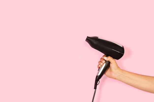 Vrouw hand met een föhn op een roze achtergrond met kopie ruimte