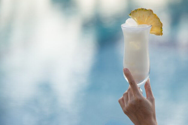 Vrouw hand met een glas cocktail aan de rand van het zwembad.