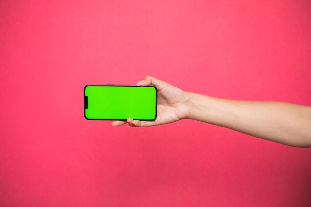 Vrouw hand met een groen scherm Smartphone op roze achtergrond.