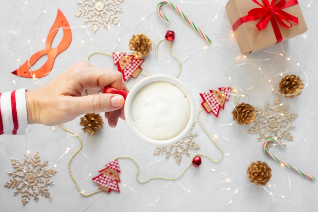 Vrouw hand met een kopje cappuccino tegen kerstversiering achtergrond.