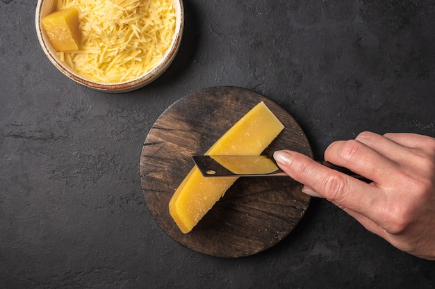 Vrouw hand met een mes snijdt een stuk Parmezaanse kaas op een houten snijplank