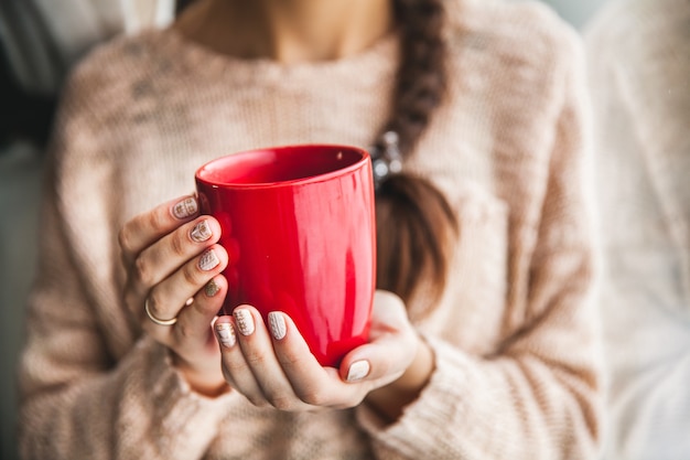 Vrouw hand met een rode kop koffie. Met een mooie wintermanicure.