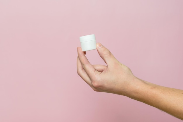 Vrouw hand met een witte pot buis met crème zalf Gezichtsverzorging fles met cosmetisch product zonder etikettering