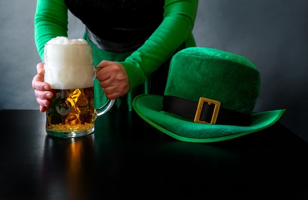 Vrouw hand met glas bier in de buurt van St. Patrick's day hoed van een kabouter op de zwarte