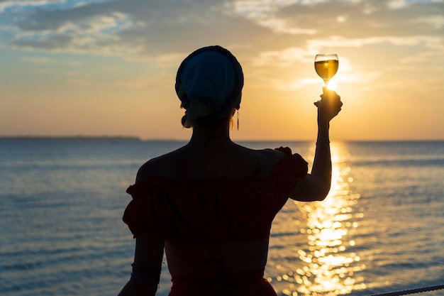 Vrouw hand met glas wijn tegen een prachtige zonsondergang in de buurt van zee op het tropische strand close-up