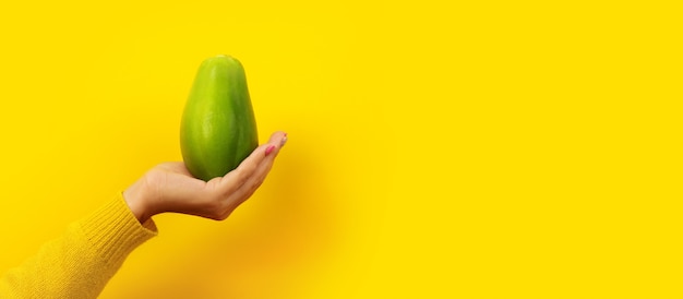 Vrouw hand met groene papaja op gele achtergrond, gezonde voeding concept