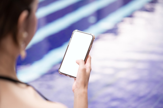 Vrouw hand met mobiele telefoon met leeg wit scherm mockup bij het zwembad.