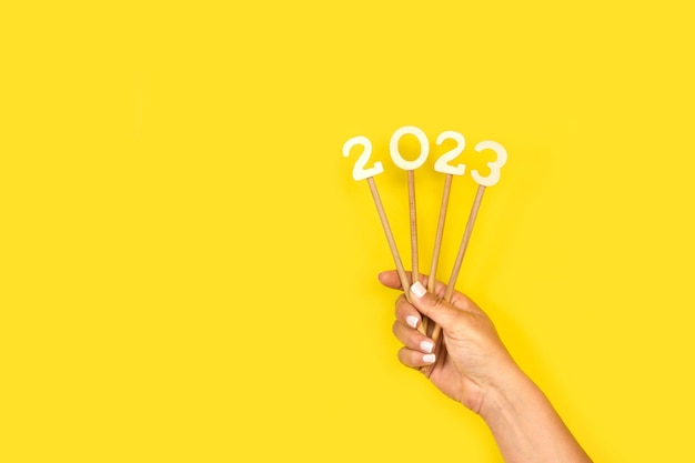 Vrouw hand met nummer 2023 op houten stokken op een gele achtergrond met kopie ruimte