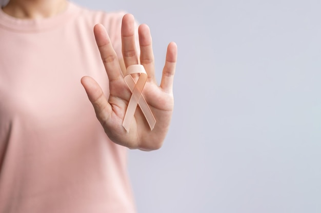 Vrouw hand met perzik lint voor september baarmoederkanker bewustzijn maand gezondheidszorg en wereld kanker dag concept