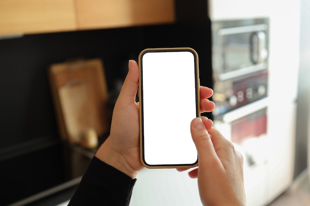 Vrouw hand met smartphone met verticaal wit scherm op keuken thuis