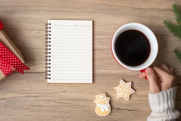 Vrouw hand met zwarte koffiekopje met lege notebook en kerstkoekjes op tafel Xmas Happy New Year doelen resolutie To do list strategie en plan concept