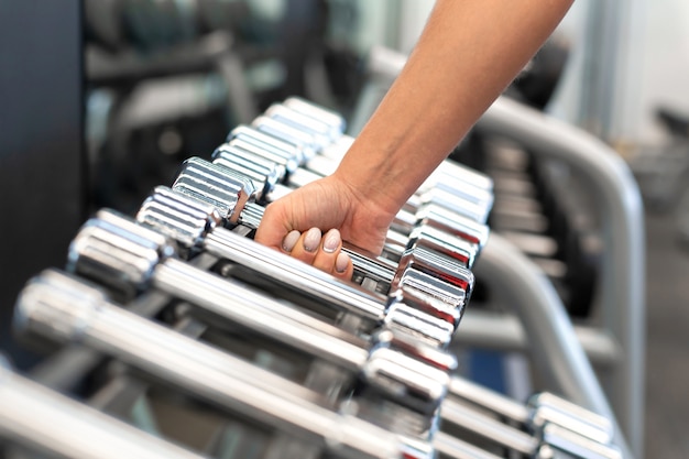 Vrouw hand neemt halter vorm rijen van halters in de sportschool