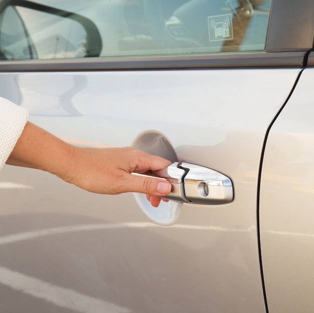 Vrouw hand opent deur van grijze metalen auto close-up