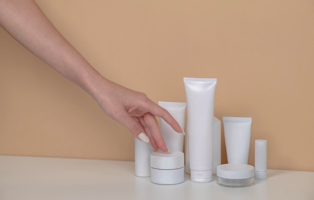 Vrouw hand pakt de lege cosmetische verpakking mockup witte tube spray fles op beige achtergrond