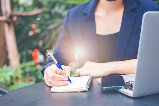 Foto vrouw hand schrijven op een notitieblok met een pen en ze houdt een mobiele telefoon op kantoor.