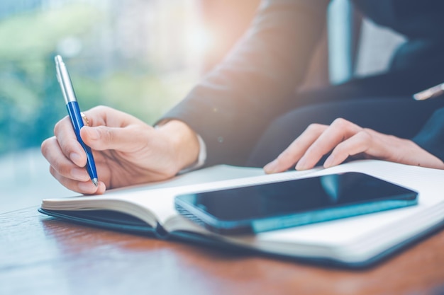 Vrouw hand schrijven op een notitieblok met een pen op kantoor er ligt een mobiele telefoon op tafel