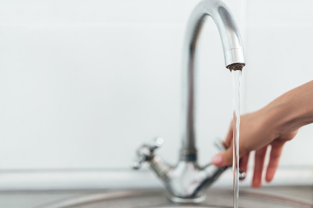 Vrouw hand zilveren kraan of waterkraan met metalen wasbak in de keuken openen.