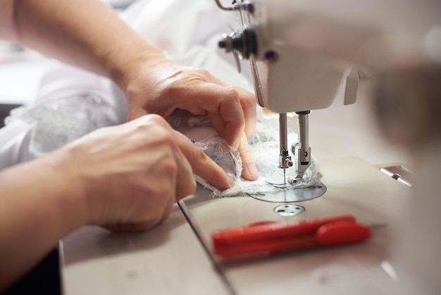 Vrouw handen bij het naaiproces en het repareren van witte stof op professionele productiemachine Close-up zijaanzicht