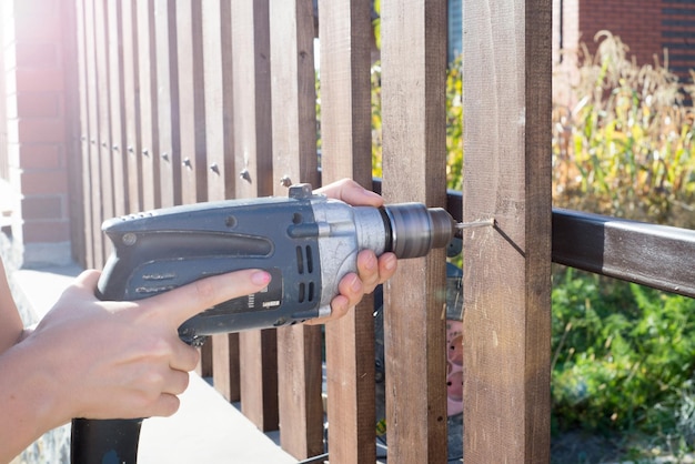 Vrouw handen boren houten plank hek aan metalen constructie Een houten hek bouwen met een boor en schroef