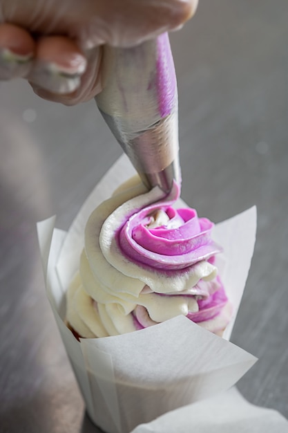 vrouw handen chef-kok met spuitzak, knijpen de room op de cupcakes.