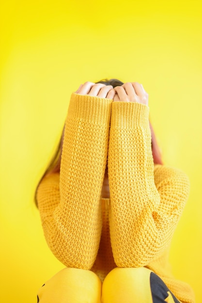 Vrouw handen in gele trui die betrekking hebben op haar gezicht geïsoleerd op gele achtergrond Gele kleur concept