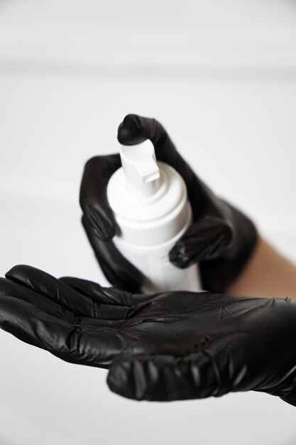 Foto vrouw handen in handschoen houdt een witte plastic fles. cosmetische procedures en producten, huidverzorging