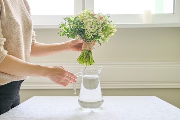 Vrouw handen met boeket bloemen in vaas op tafel