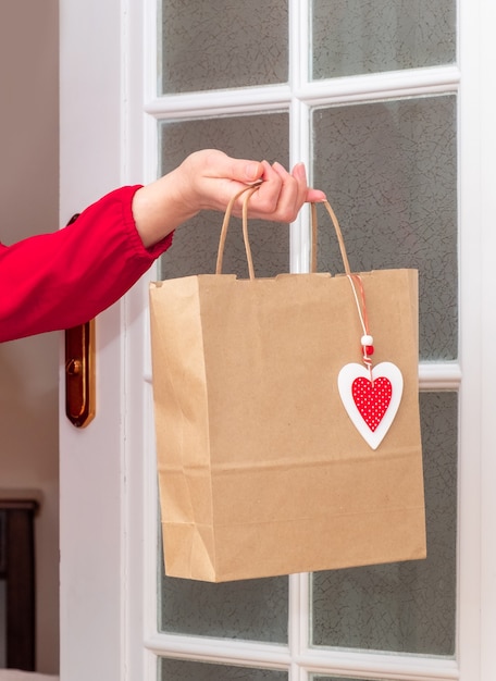 Vrouw handen met boodschappentas met rode harten van valentijnsdag in de buurt van de witte deur.