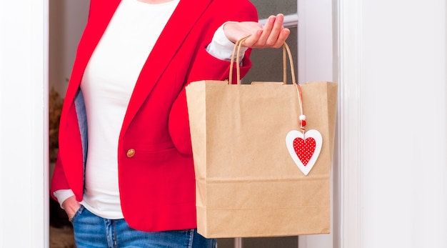 Vrouw handen met boodschappentas met rode harten van valentijnsdag in de buurt van de witte deur.