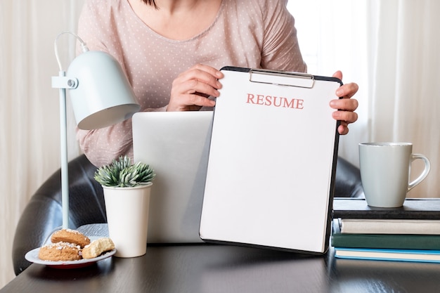 Vrouw handen met CV-applicatie in de buurt van haar werkplek met laptop.