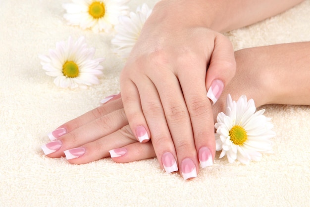 Vrouw handen met Franse manicure en bloemen op handdoek