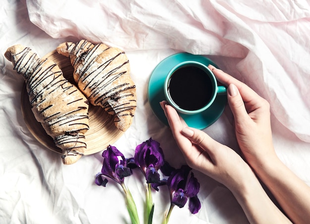 Vrouw handen met kopje koffie in bed. Mooie bloemen en een horloge met armband