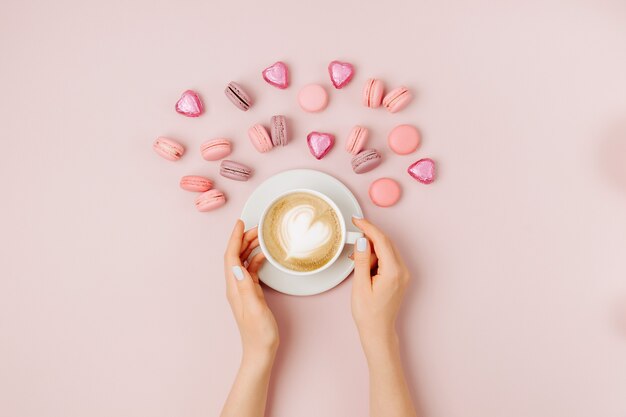 Vrouw handen met kopje koffie op bleke roze achtergrond. Platliggend, bovenaanzicht