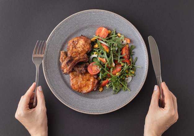 Vrouw handen met mes en vork voorbereiden om te proeven van de heerlijke gebakken varkensribbetjes met verse groentesalade Bovenaanzicht