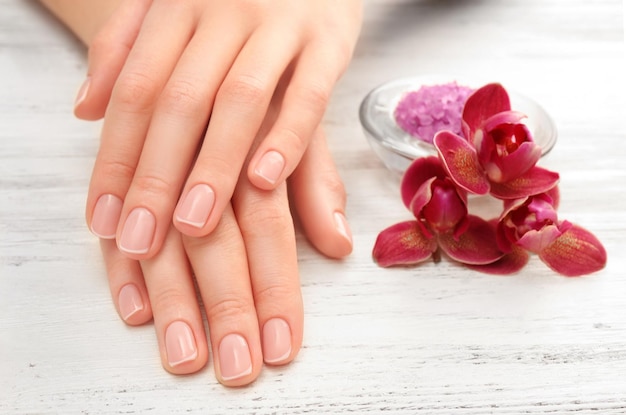 Vrouw handen met mooie manicure en paarse orchidee op houten achtergrond close-up