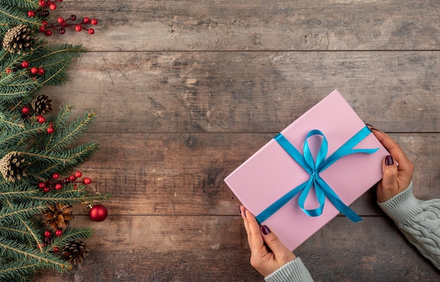 Vrouw handen met roze kerstcadeau of huidige doos versierde dennenboom Vrouwelijke handen in trui