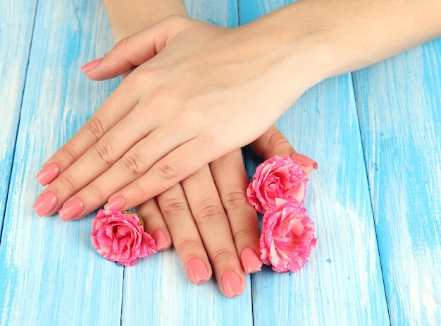 Vrouw handen met roze manicure en bloemen op een houten achtergrond kleur