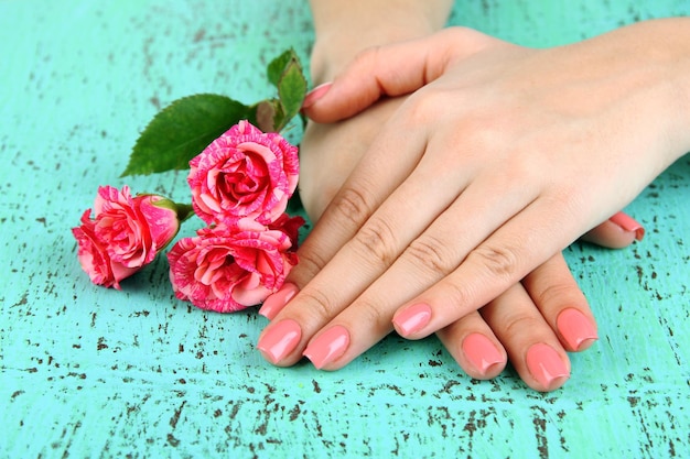 Vrouw handen met roze manicure en bloemen op kleur achtergrond