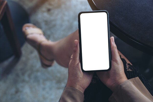 Vrouw handen met zwarte mobiele telefoon met leeg wit scherm zittend in café